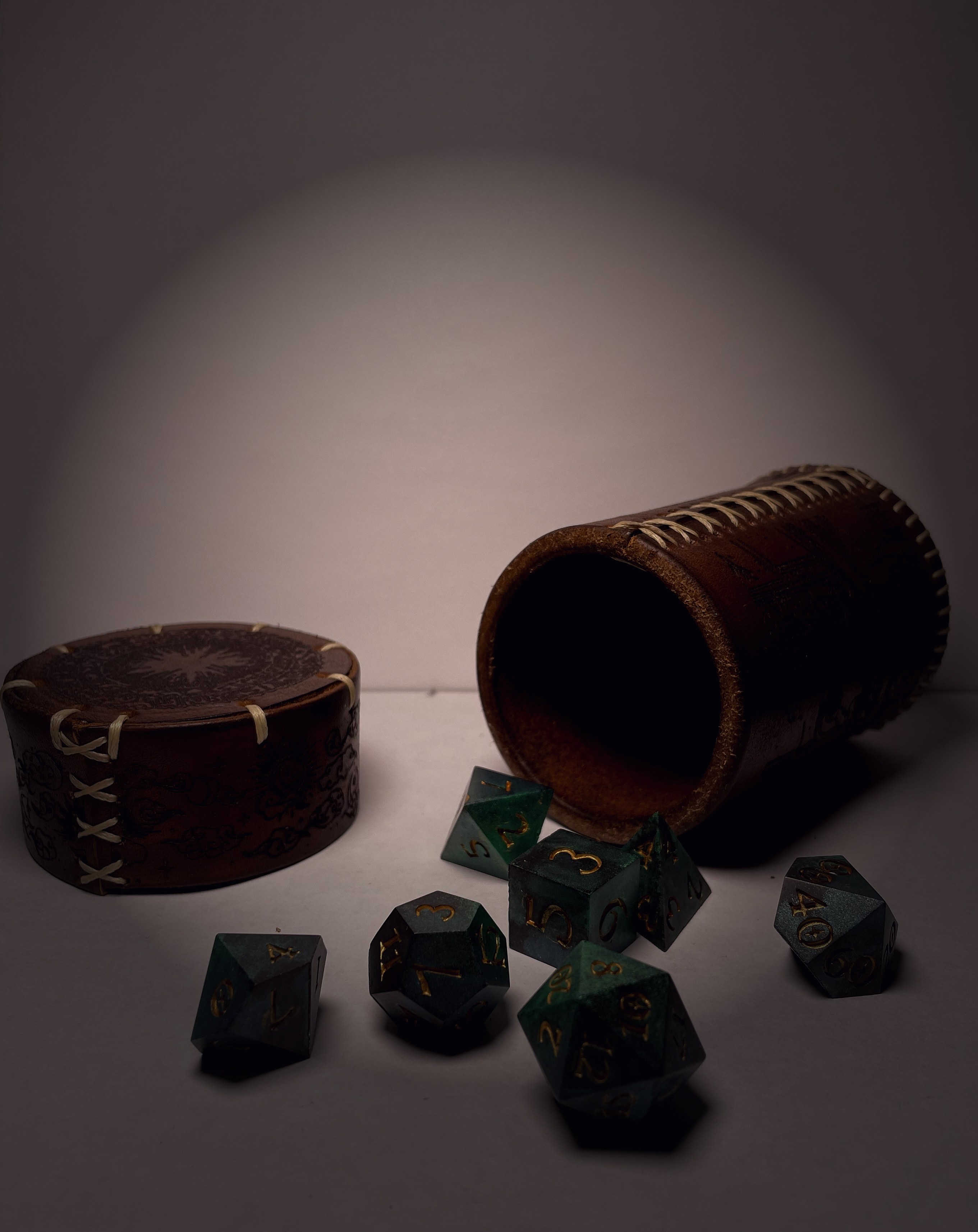 Leather dice cup open with a full set of composite dice spilled across the table
